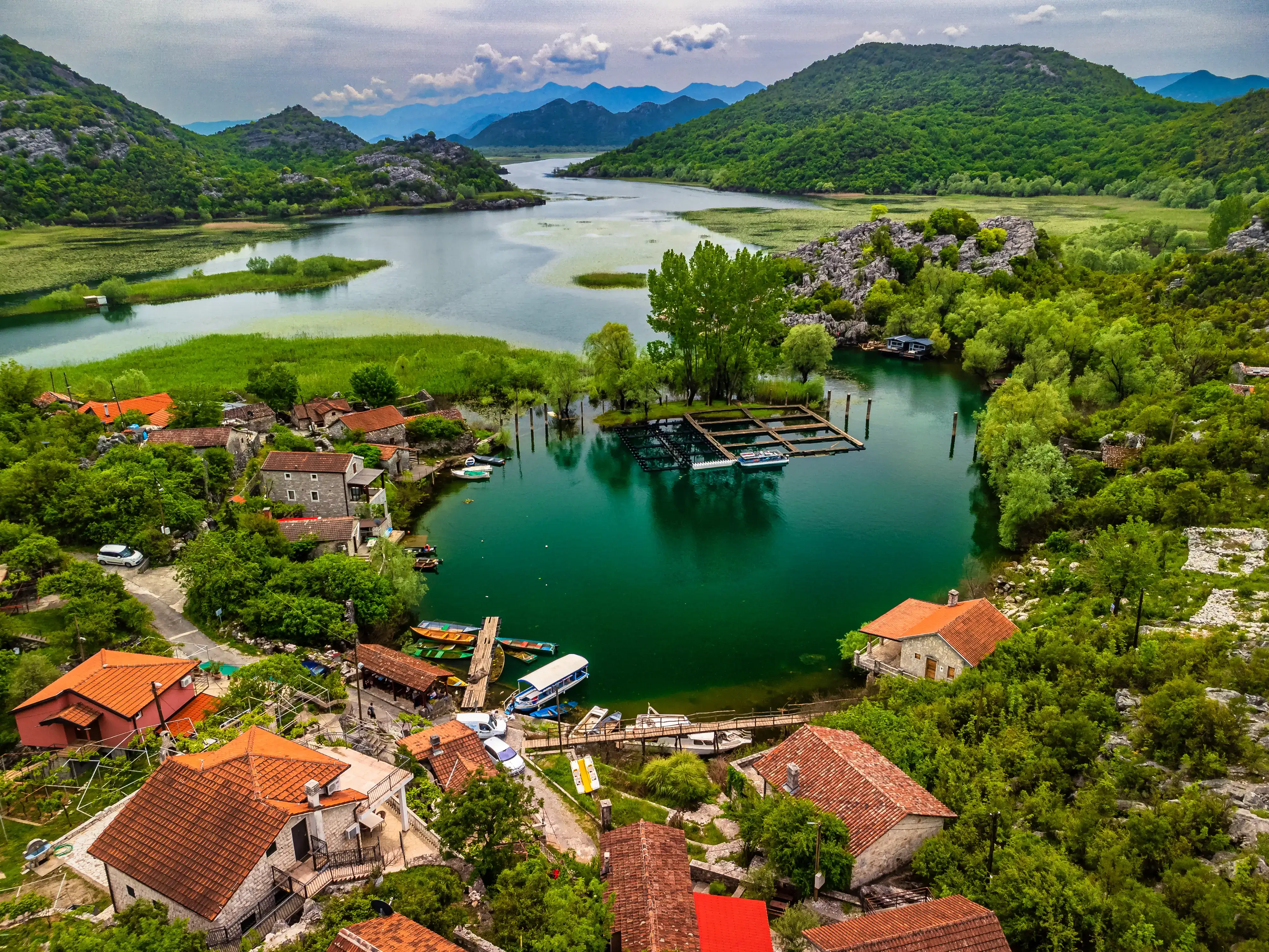 Wooden boat gliding across mirror-still Skadar Lake at sunset with the Rumija mountains behind